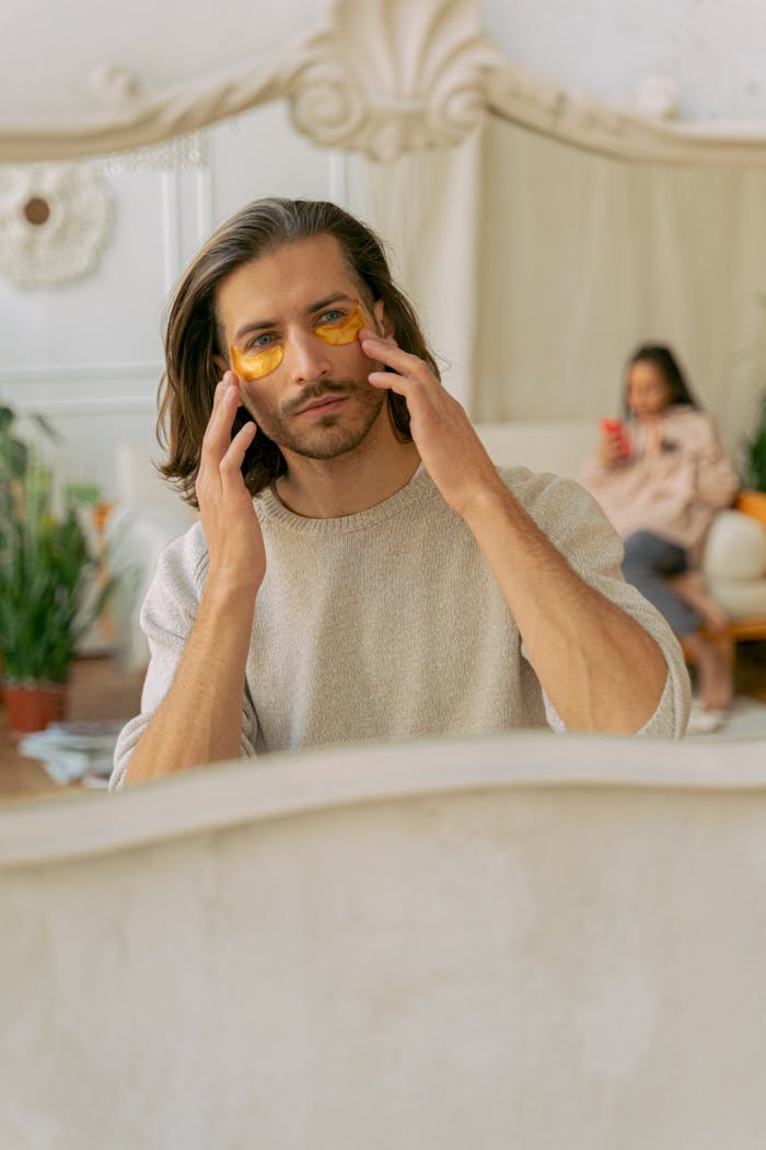 A man applying under-eye patches, enjoying a beauty treatment indoors.